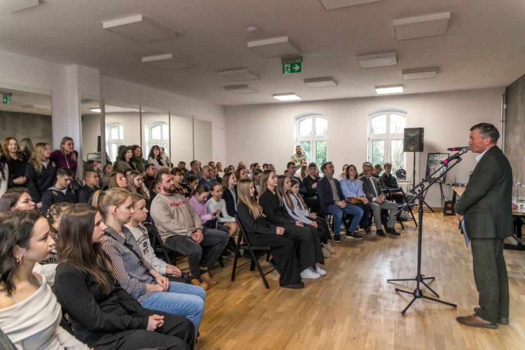 Mężczyzna przemawia do publiczności w jasnym pomieszczeniu