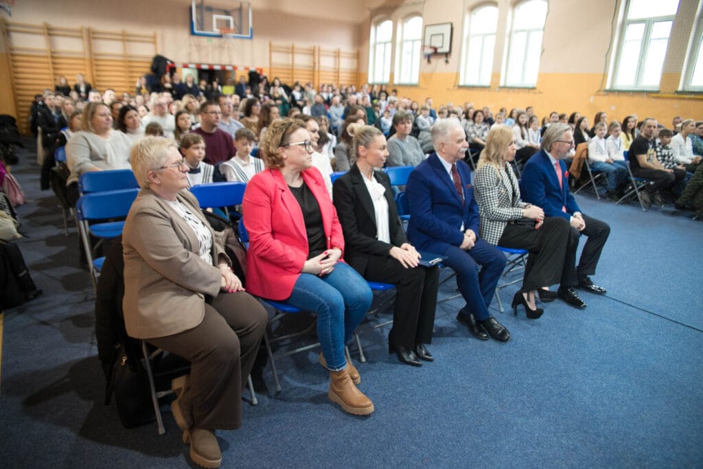 Grupa ludzi siedzi na krzesłach podczas spotkania szkolnego